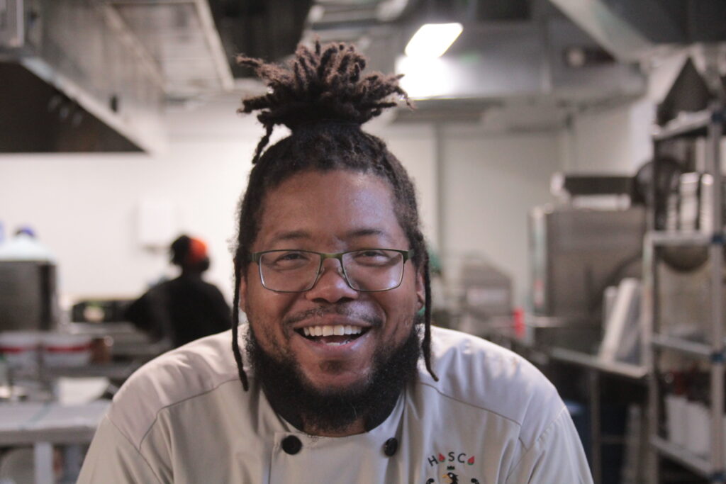 Man wearing chef jacket smiling in a commercial kitchen